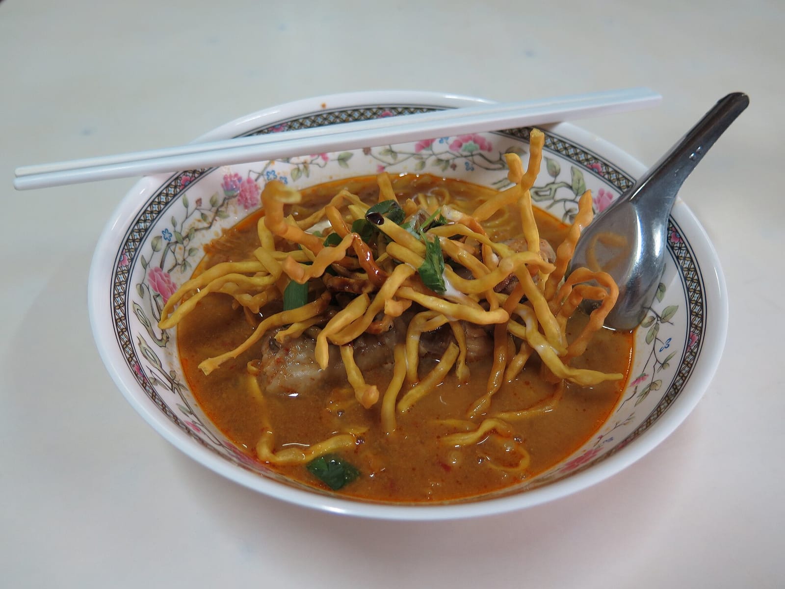 A bowl of khao soi with pickled greens and lime