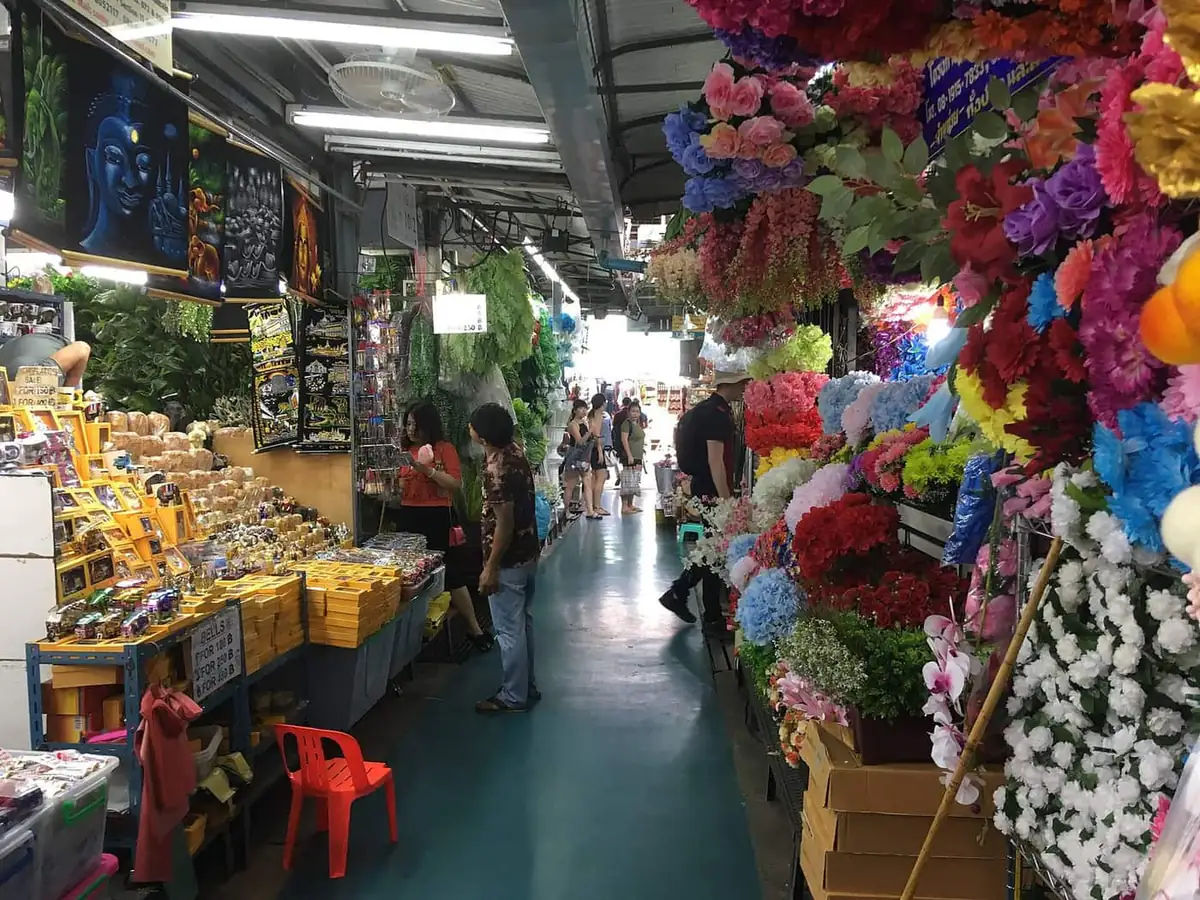 A covered aisle of stalls at Chatuchak Weekend Market in Bangkok, with prices on the signs